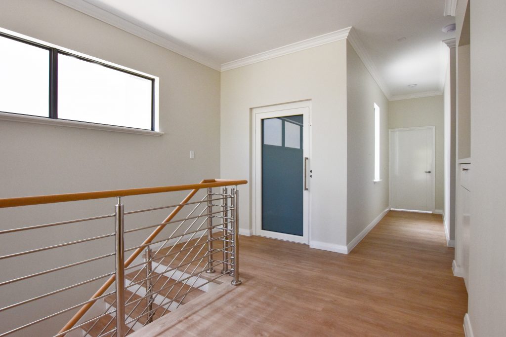 Residential lift with white framed door in Applecross. Located next to stairs.