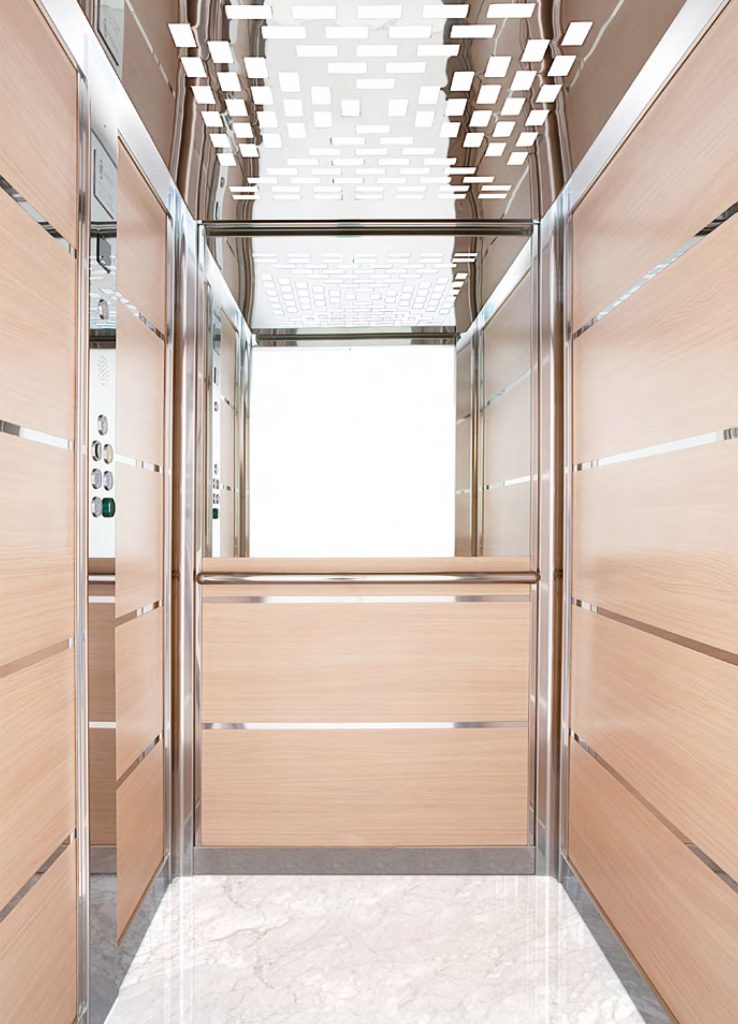 a spacious lift cabin with wooden walls, silver panelling, marble floors, half heigh mirror and patterned light display.