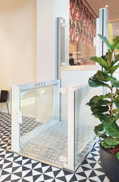 a white mini lift with grey metal floors sits on top patterned tiles inside a building.