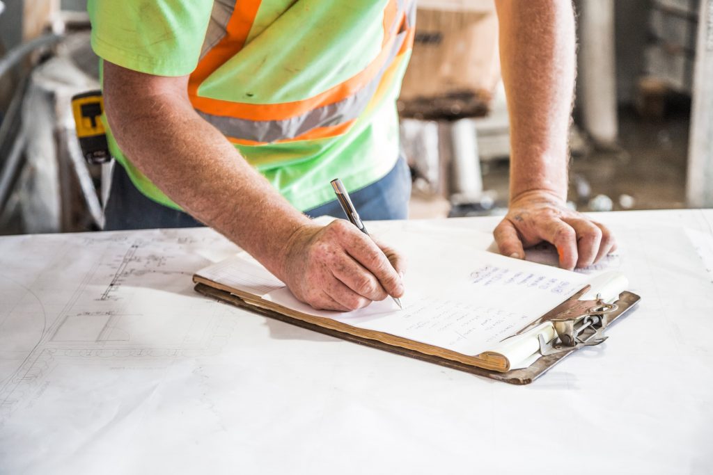 a workman in a hi-vis shirt writes on a project sheet in a worksite.