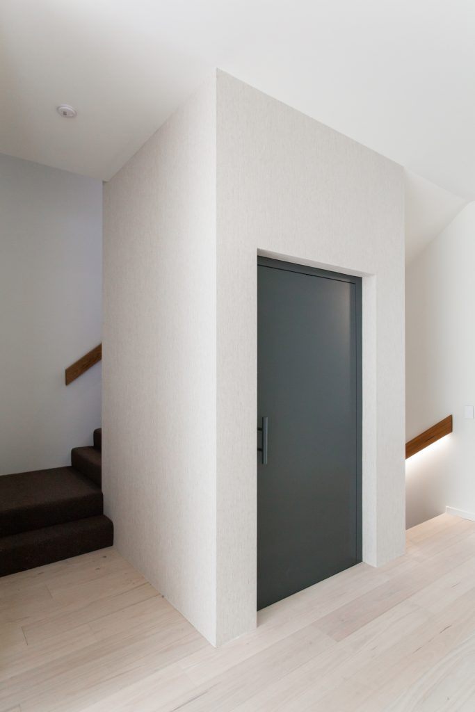 a white elevator shaft with a closed blue door elevator next to a staircase in a house