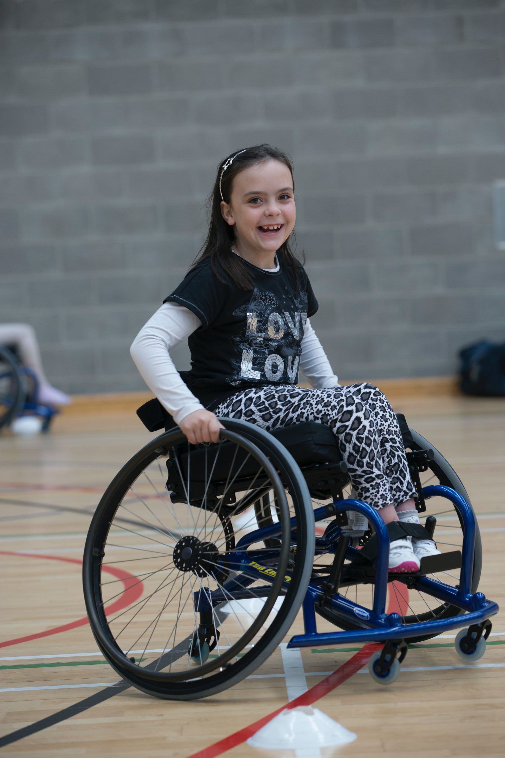 a child who is using a wheelchair is playing on the school indoor basketball court