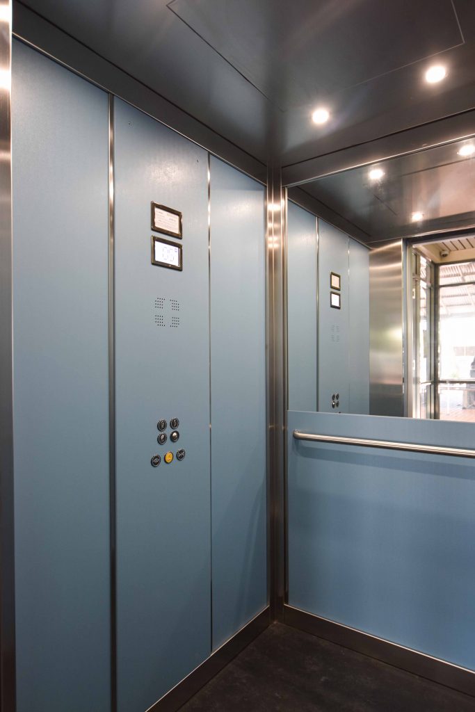 cabin of a school elevator with a digital control panel and buttons. dda complaint features and a half length mirror on the back wall.