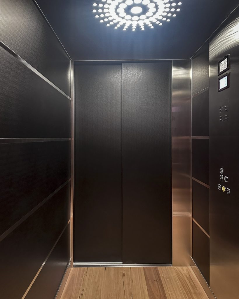 Modern elevator interior with wooden floor and lighting.