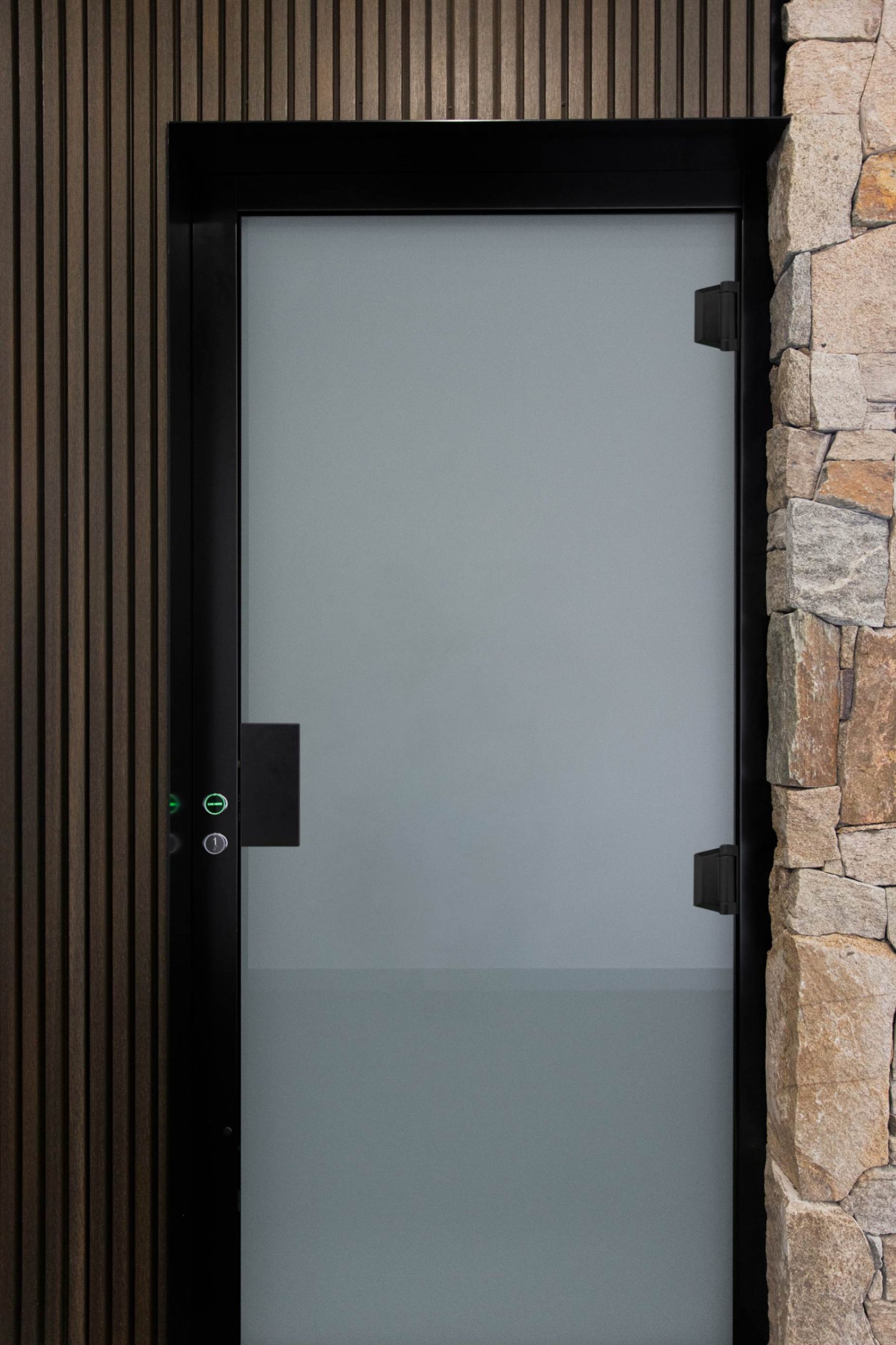 20250408 Modern glass door with stone and wood panels.