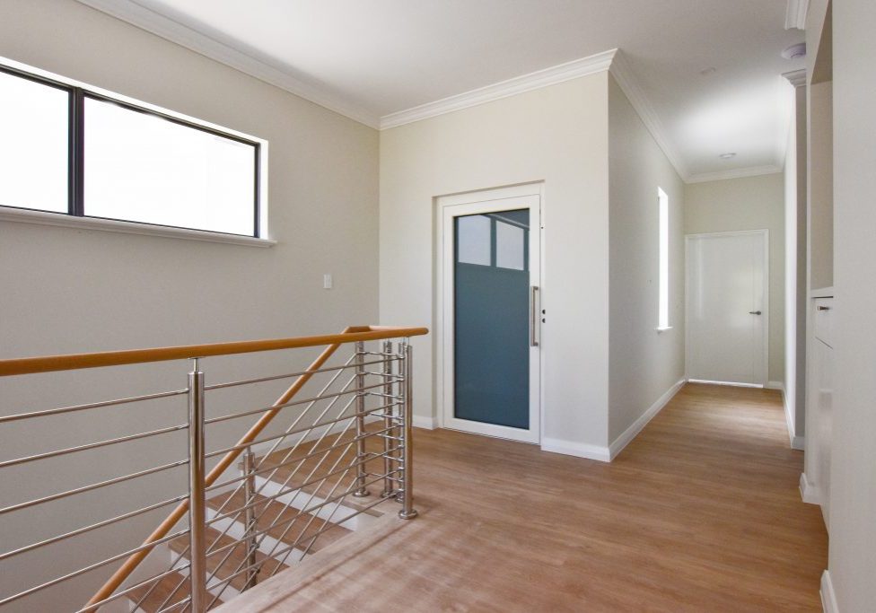 Residential lift with white framed door in Applecross. Located next to stairs.