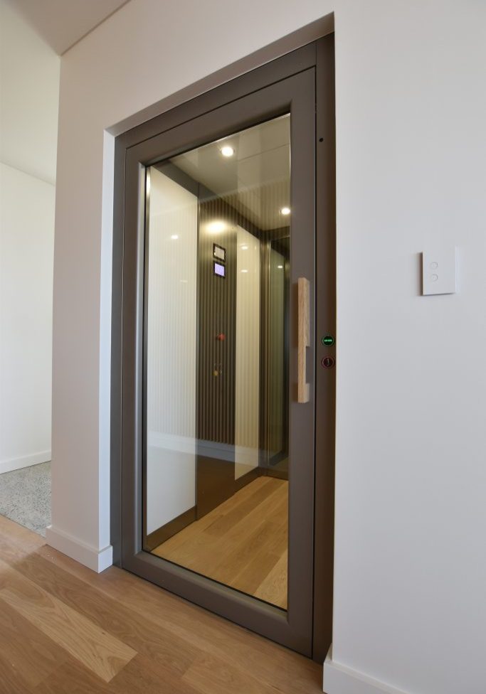 a modern lift with a clear door and wooden floors.