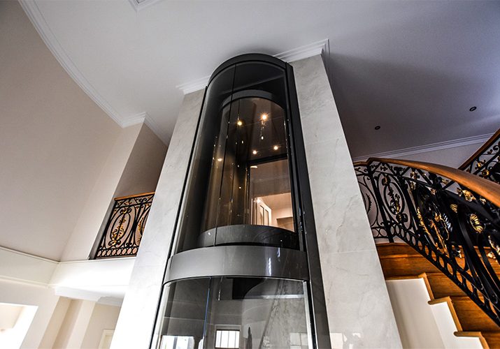 matte black and glass round home lift adjacent to spiral staircase