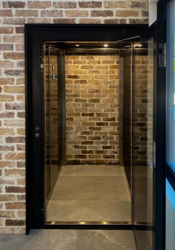 Modern glass home lift against exposed brick wall