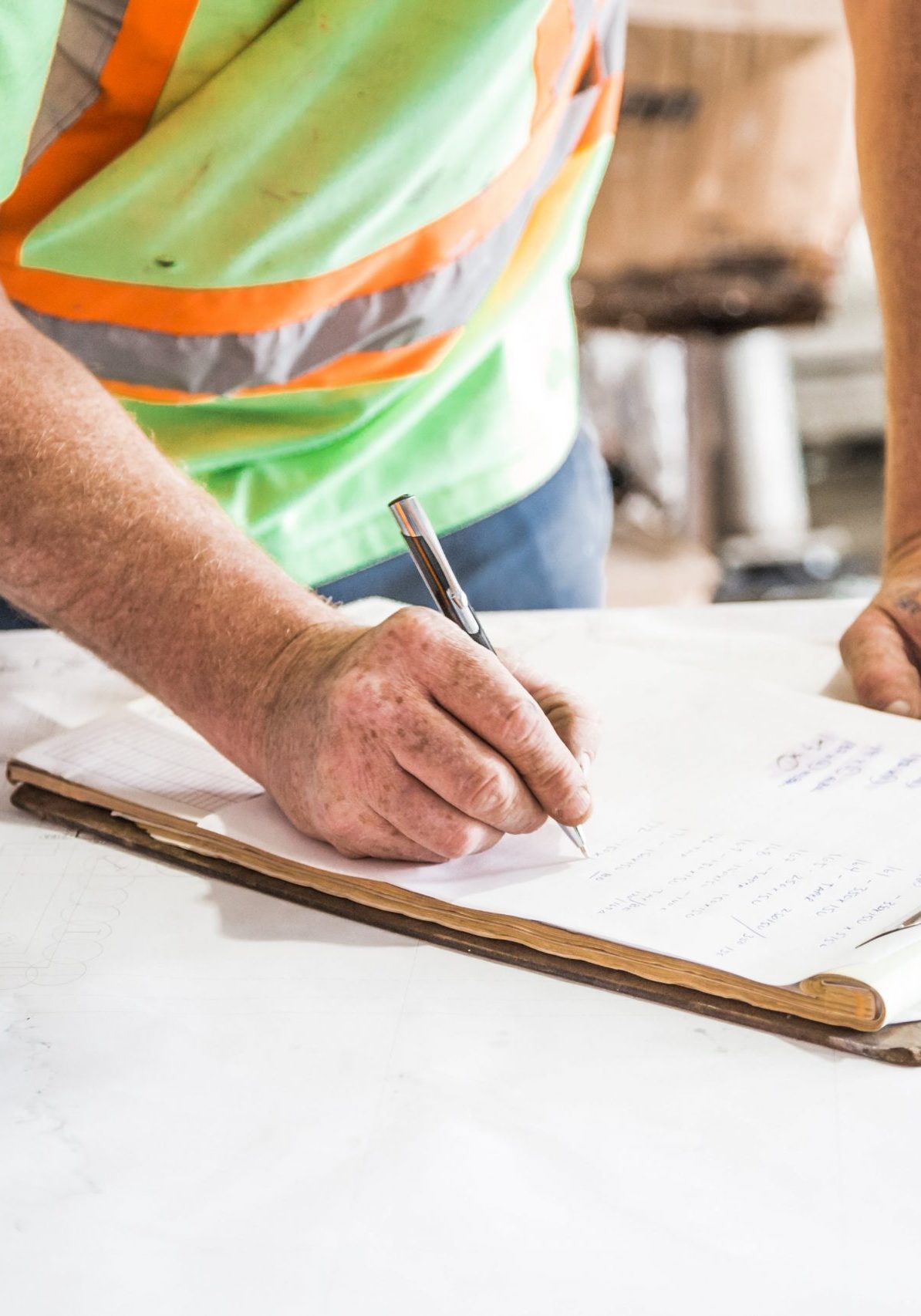 A buyers guide to lift installation and servicing a workman in a hi-vis shirt writes on a project sheet in a worksite.