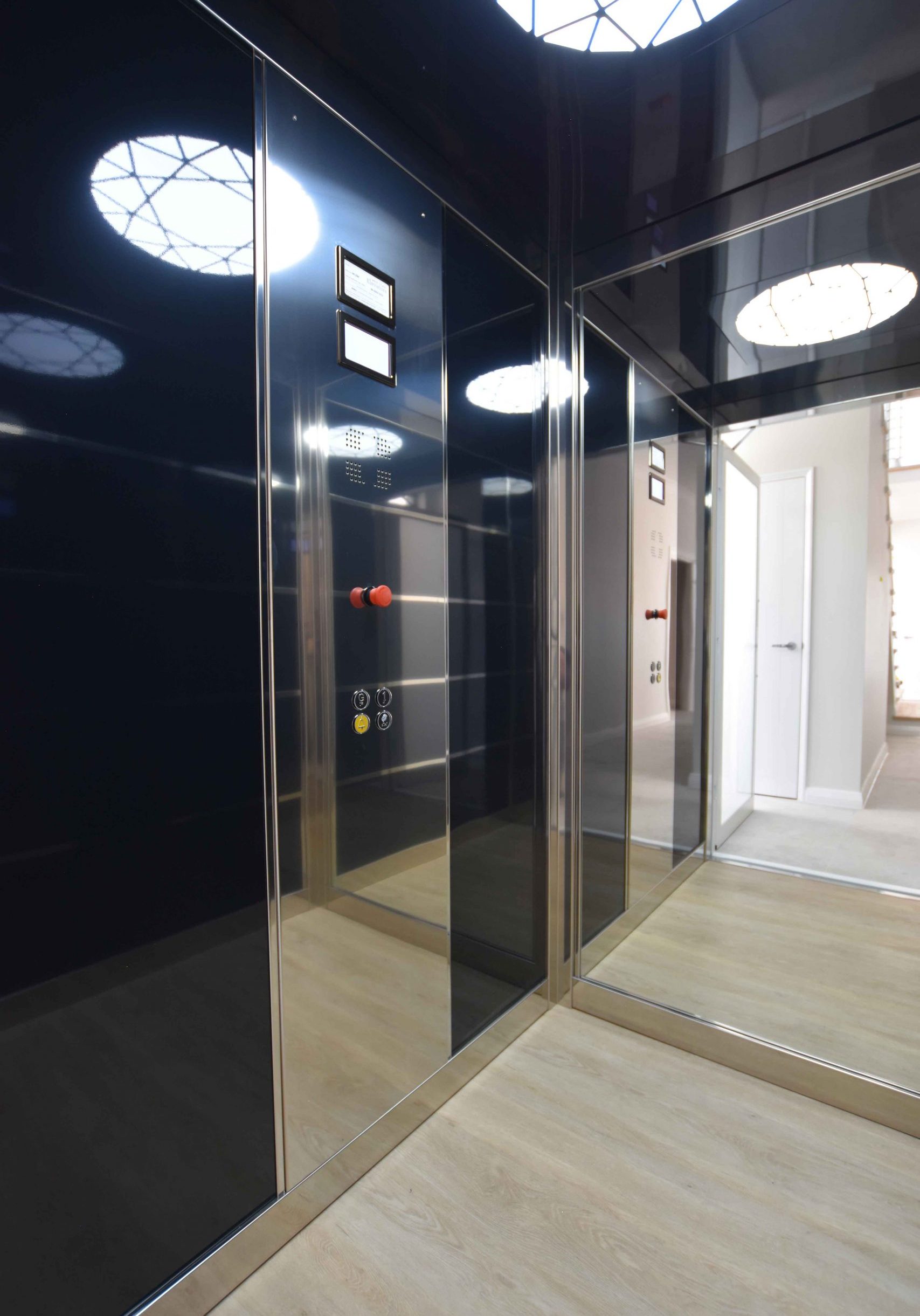 Inside of sovereign lift, with one large light, light wood floors, black features and reflective back wall.