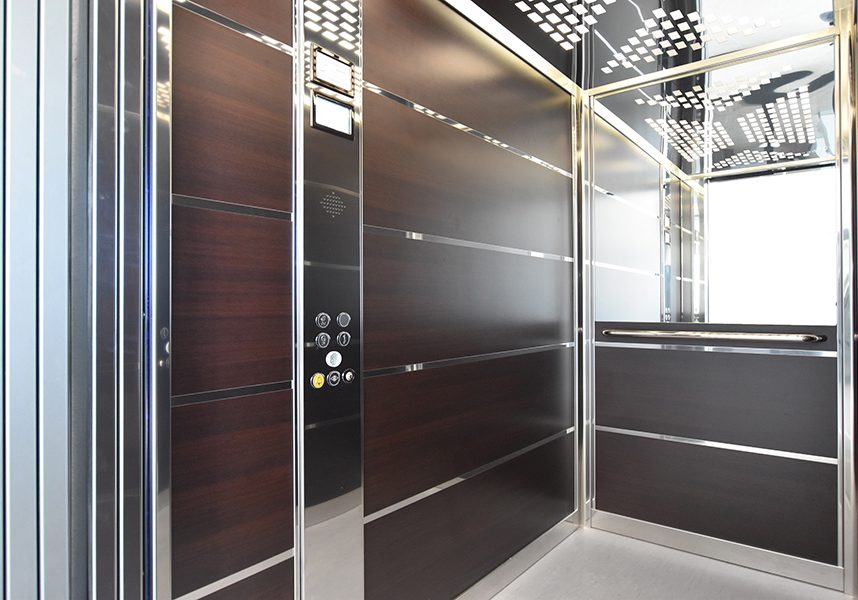 commercial lift with brown panel walls, a mirror at the back and silver details.