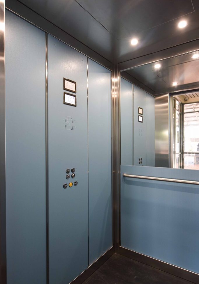 cabin of a school elevator with a digital control panel and buttons. dda complaint features and a half length mirror on the back wall.